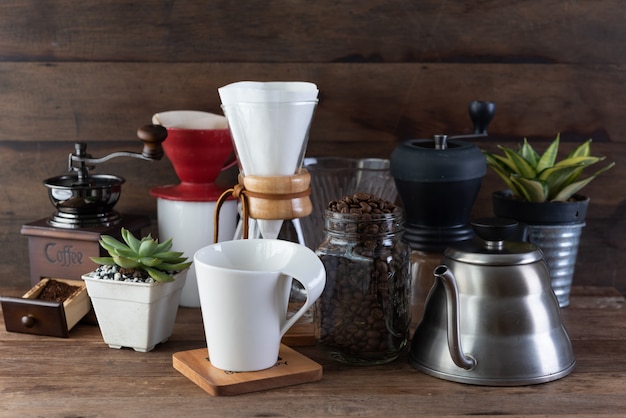 Foto gocciolamento del caffè messo con, fagioli arrostiti, bollitore, smerigliatrice, tazza bianca e vaso di fiori sulla tavola e sul fondo di legno