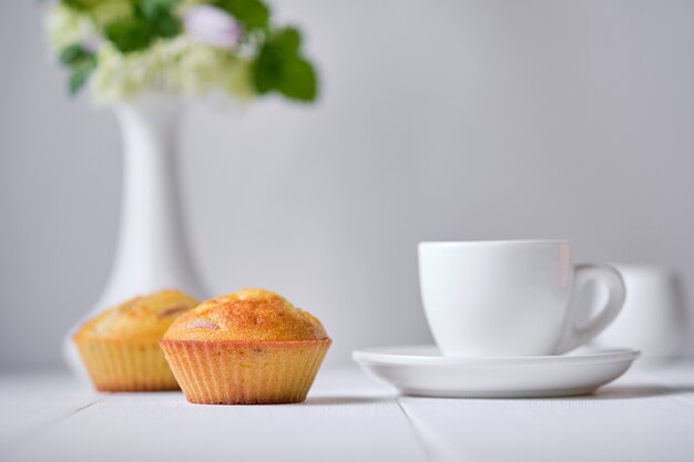 朝食に新鮮な桃とコーヒーとフルーツのマフィン。白い木製のテーブルの上に花瓶にデザート、エスプレッソ、花と朝のテーブル。