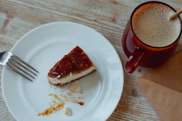 Coffee in a glass cup and nutty cheesecake on a white plate stand on a wooden table