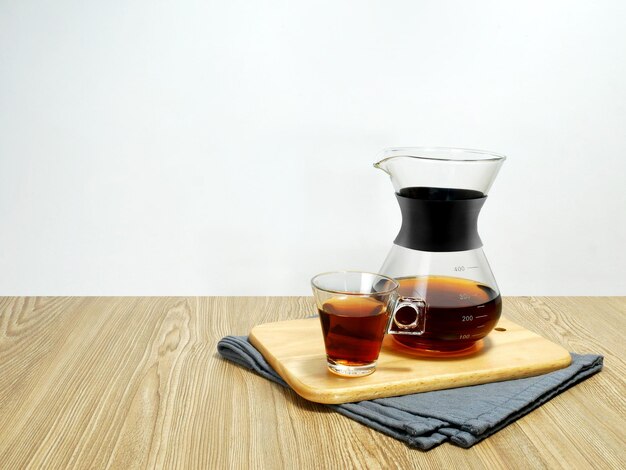 Coffee in a glass jug and cup on tray on wooden texture background