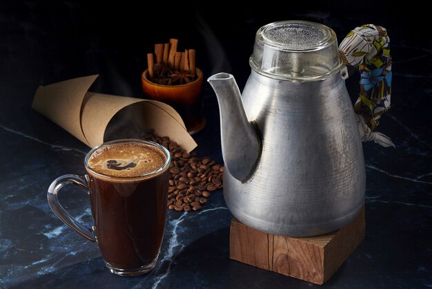 Coffee in a glass mug and a vintage aluminum geyser coffee maker on a dark background with coffee beans