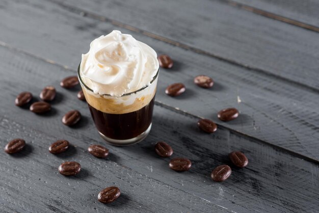 A coffee in glass with cream on the top on wooden background