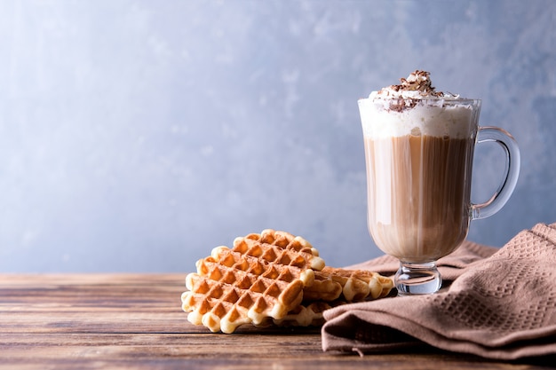 Coffee glass with whipped cream and Viennese waffles on a wooden table.