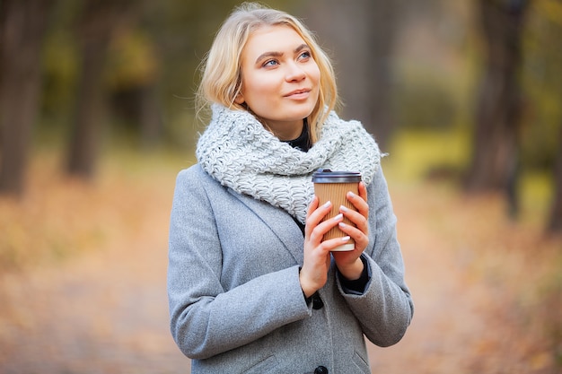 行くコーヒー。秋の公園でコーヒーを持つ若い女性