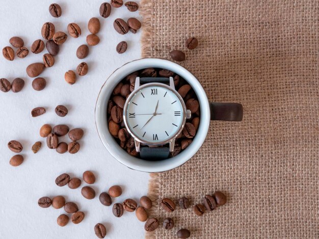 Coffee grains are scattered on a canvas napkin and a hand clock in a cup coffee time lunch