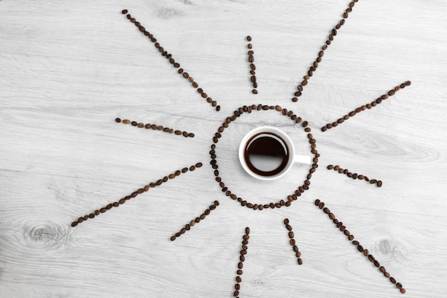 Coffee grains folded in the form of the sun on a wooden . In the middle is a cup of coffee, meaning it's time to drink coffee after sunrise