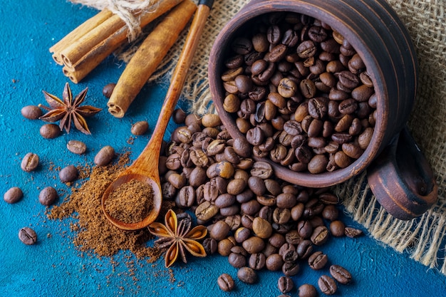 Coffee grains pouring out of a clay cup and scattered on a blue textural background