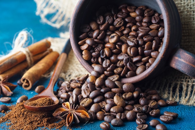 Coffee grains pouring out of a clay cup  and scattered on a blue texture