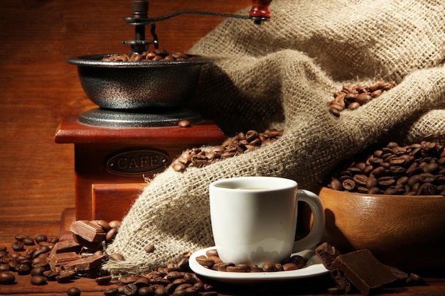 Coffee grinder and cup of coffee on brown wooden background