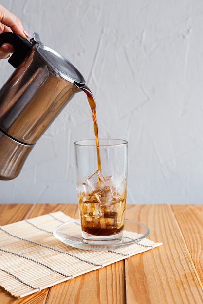 Coffee is poured into a glass with ice