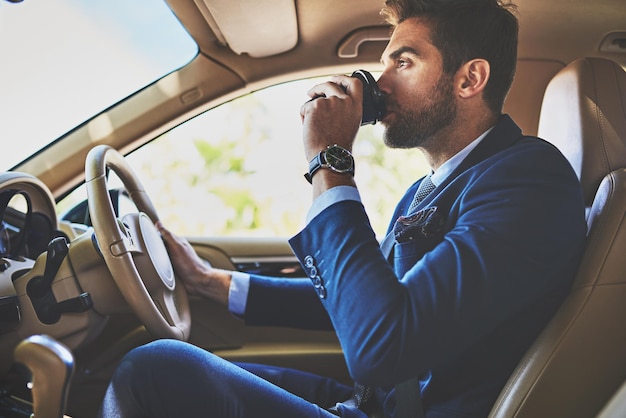 Il caffè lo fa andare avanti inquadratura di un giovane uomo d'affari allegro che guida nella sua macchina per lavorare mentre è seduto nel traffico e beve caffè