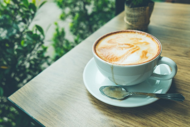 Coffee latte art with small tree on the wooden desk in coffee shop vintage color tone