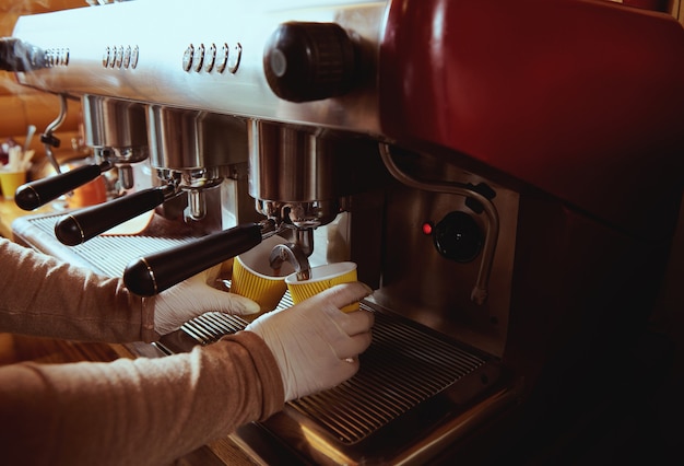 Coffee machine pourig coffee to yellow cardboard coffee cup in bar. Cropped image. Closeup