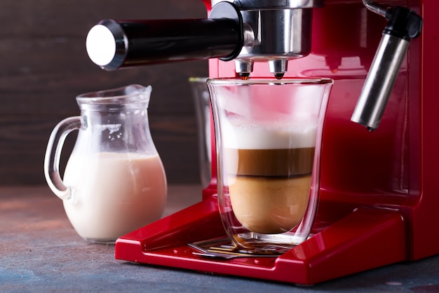 Coffee machine preparing fresh latte coffee and pouring into glass at restaurant, close up