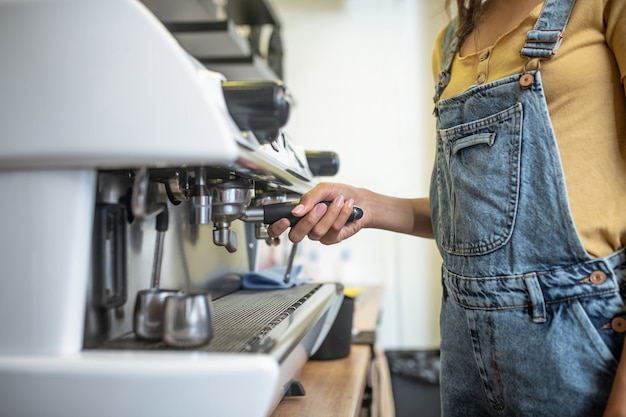 コーヒーメーカー。カフェのコーヒーメーカーの女性の細い手持ちレバー、顔が見えない