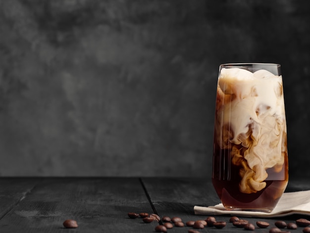 Coffee and milk are mixed in a highball glass with ice. Gray wooden table.  