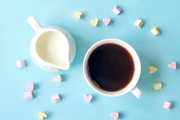 Coffee and milkman with milk on a blue surface with many sweet hearts, top view