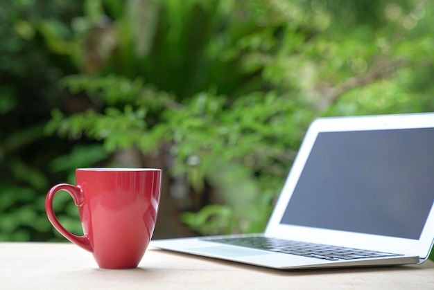 Coffee morning in red cup with computer laptop green garden bokeh background