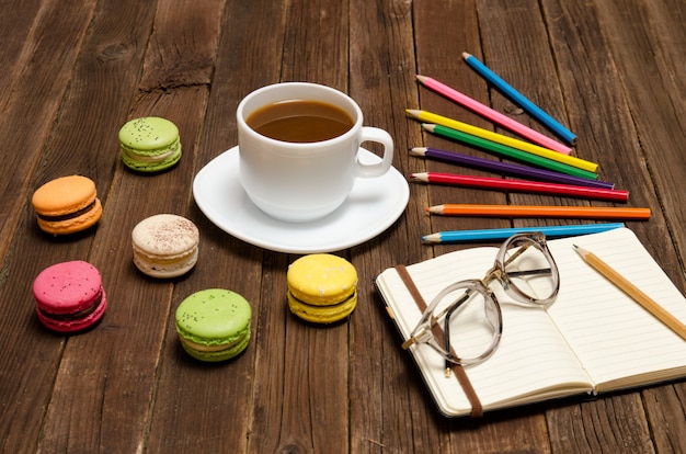 Coffee mug, macarons, colored pencils and a notepad with glasses