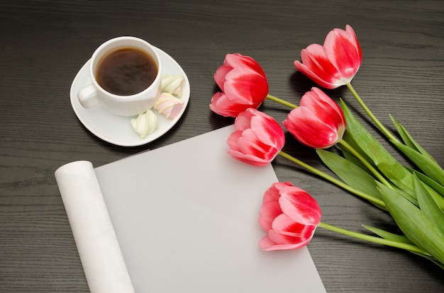 Coffee mug, marshmallow, clean sheet and pink tulips. Black table. top view