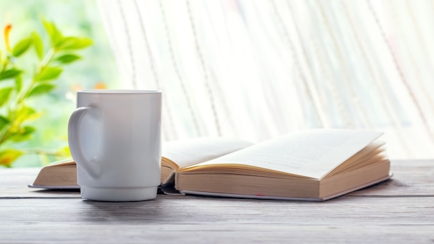 Coffee mug near an open book and flowerpot
