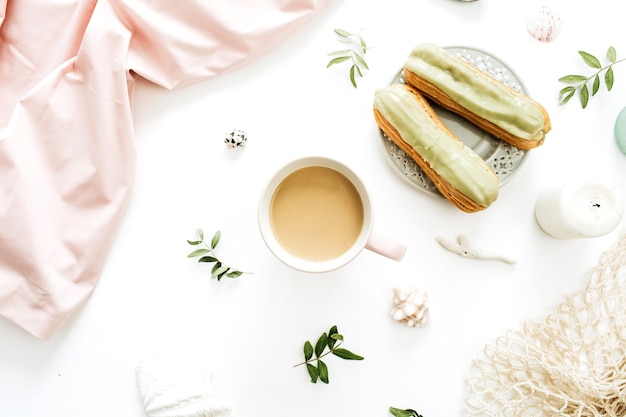 Coffee mug, pistachio cakes, pink blanket, string bag, seashells on white background. flat lay, top view