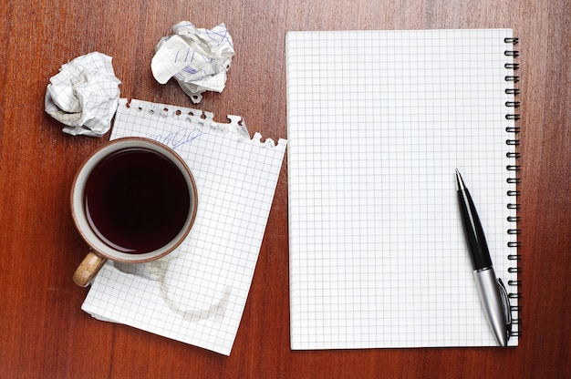 Coffee notebook pen and crumpled paper on table