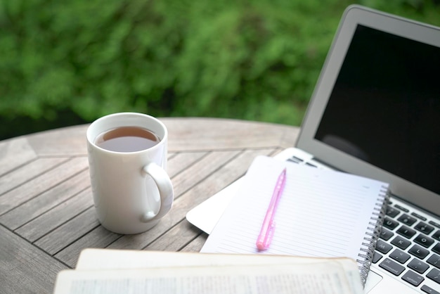 Coffee notepad book pen and computer laptop on table with green plants at the background