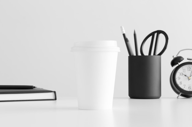 흰색 테이블에 노트북 시계와 작업 공간 액세서리가 있는 커피 종이 컵 모형