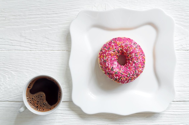 Coffee and pink donut on table