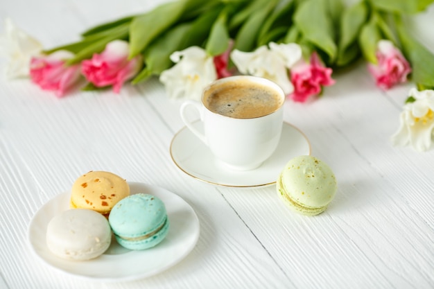 Coffee, pink and white tulips and macarons on the white wooden table. Breakfast. Coffee break.