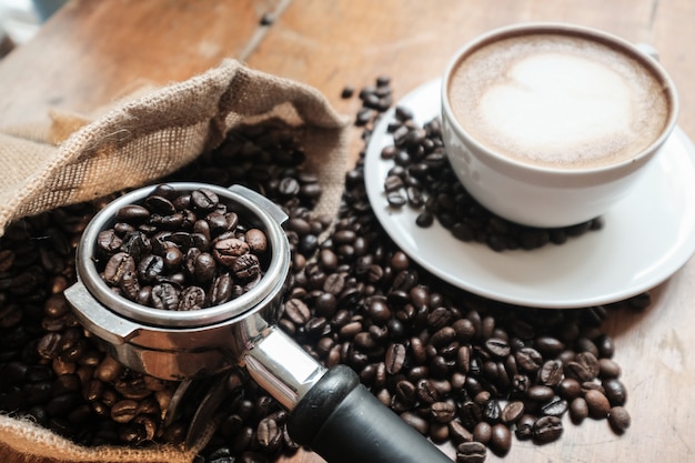 Coffee portafilter filled with coffee beans with a cup of coffee latte