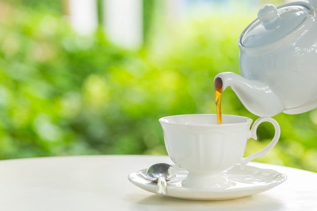 coffee pot pouring hot coffee into a cup during breakfast in morning sunlight 