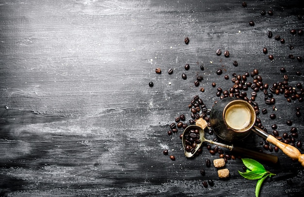 Coffee pot with coffee beans, cane sugar and fresh leaves. On a black chalkboard.