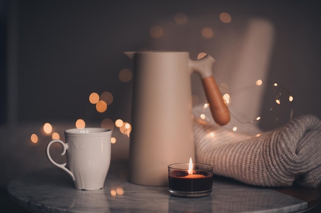 写真 寝室のクリスマス ライトの上に大理石のテーブルに香りのキャンドルを燃やす紅茶のカップとコーヒー ポット居心地の良い家の雰囲気