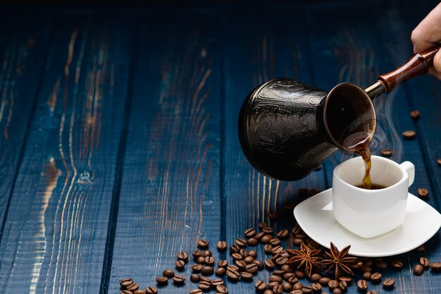 Il caffè si versa in una tazza su un tavolo di legno blu con chicchi di caffè.