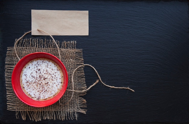 Coffee in red cup on rustic burlap and blank paper card