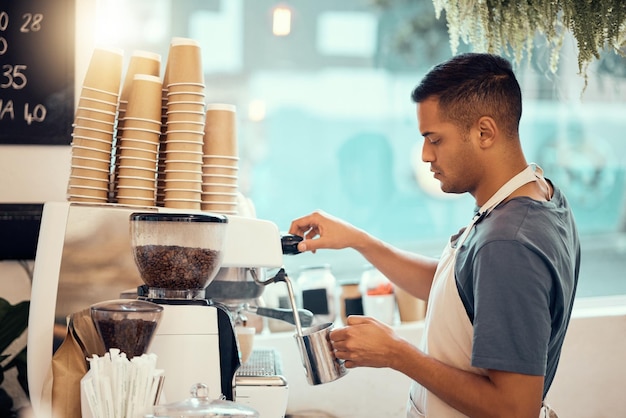 Coffee shop barista and service with a man at work using a machine to pour a drink in the kitchen Cafe small business and waiter with a male employee working in a restaurant to prepare a beverage
