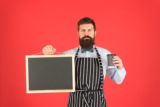 Coffee shop - small business. serious barista man with beard. hipster professional barista in apron uniform. take away coffee here. profitable proposition. copy space on board.