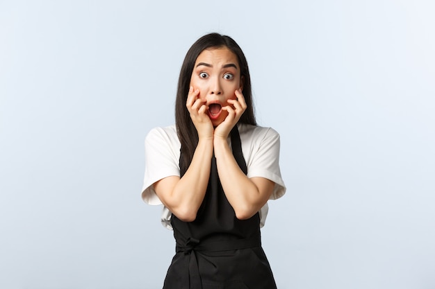 Coffee shop, small business and startup concept. Scared young woman screaming staring ambushed at something scary, hold hands near opened mouth, wearing cafe black apron uniform