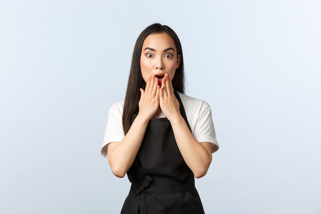 Coffee shop, small business and startup concept. Shocked young female staff at cafe gasping over shocking gossip, standing with opened mouth and staring camera, white background