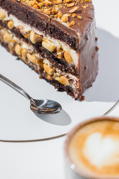 Caffè, cucchiaio, una fetta di torta sul piatto su fondo bianco.