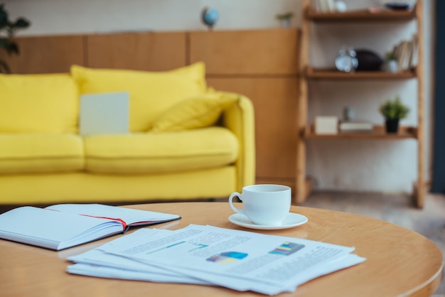 Журнальный столик с бумажной чашкой кофе и блокнотом в гостиной