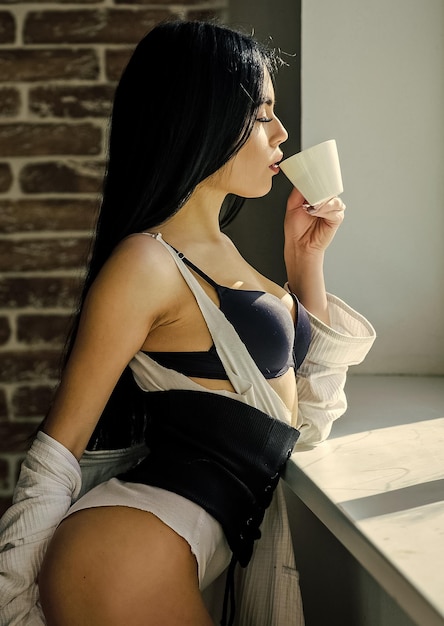 Coffee take me away Sensual girl drinking her favorite morning coffee Pretty woman drinking fresh hot coffee at window Sexy girl holding ceramic coffee cup