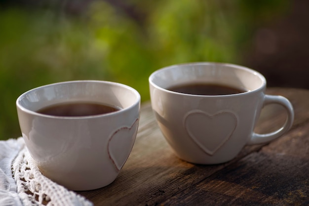 Coffee, tea in cups with heart decor, lace napkin on a wooden table. Outdoor brunch refreshments.