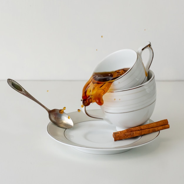 Caffè o tè che si rovescia dalla tazza della porcellana su fondo bianco. immagine quadrata. concetto di colazione