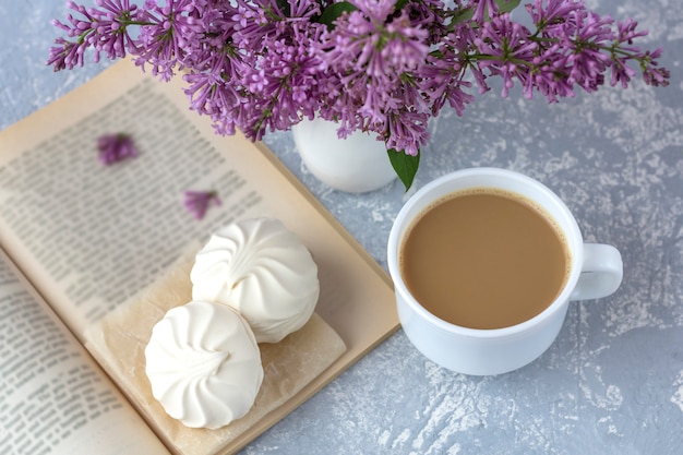 Coffee or tea with milk and marshmallows. Reading a book in the garden with a cup of coffee. Romantic still life with lilac flowers.