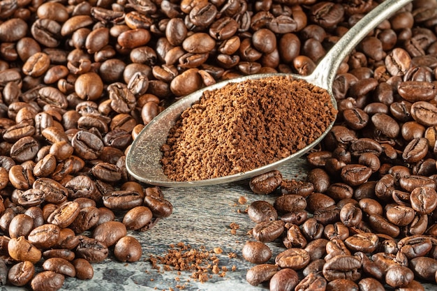 Тема кофе Лыжка, наполненная измельченным кофе, лежит среди кучи кофейных зерен