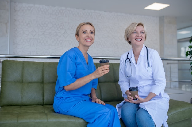 Coffee time. Two female doctors sitting on sofa, enjoying coffee