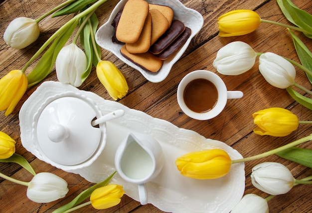 Coffee tray between white and yellow tulips on wooden table top view